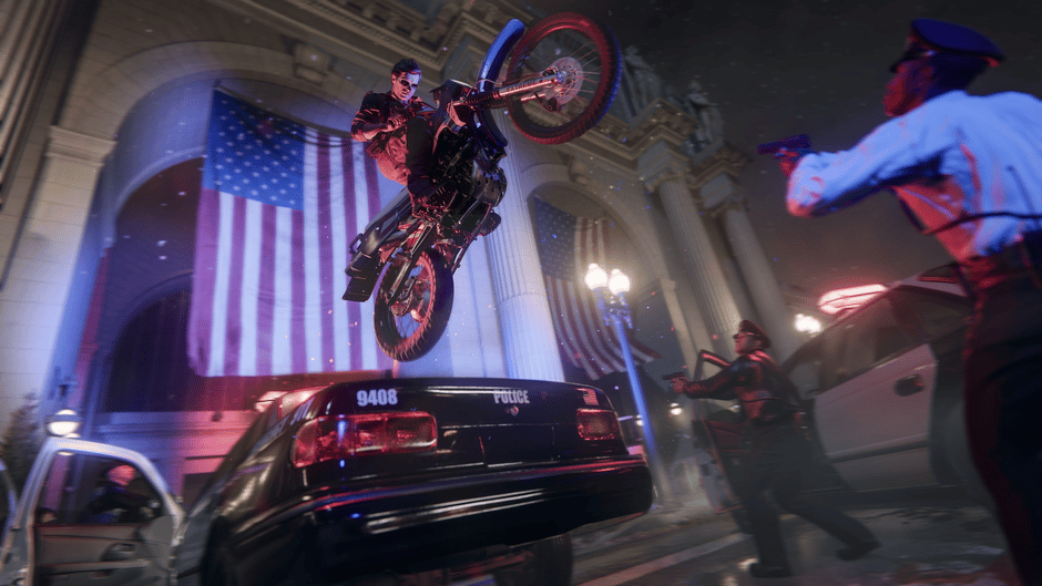 Motorcyclist jumps over a police car in a dramatic action scene, set against an American flag-lit urban backdrop at night.